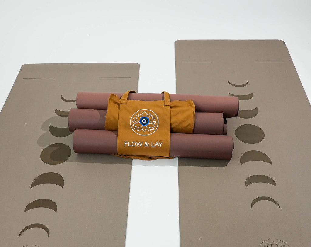A set of rolled Red Rocks Sedona colored yoga mats with phases of the moon print, bundled with a tan colored tote bag featuring the 'FLOW & LAY' logo, on a clean white background.