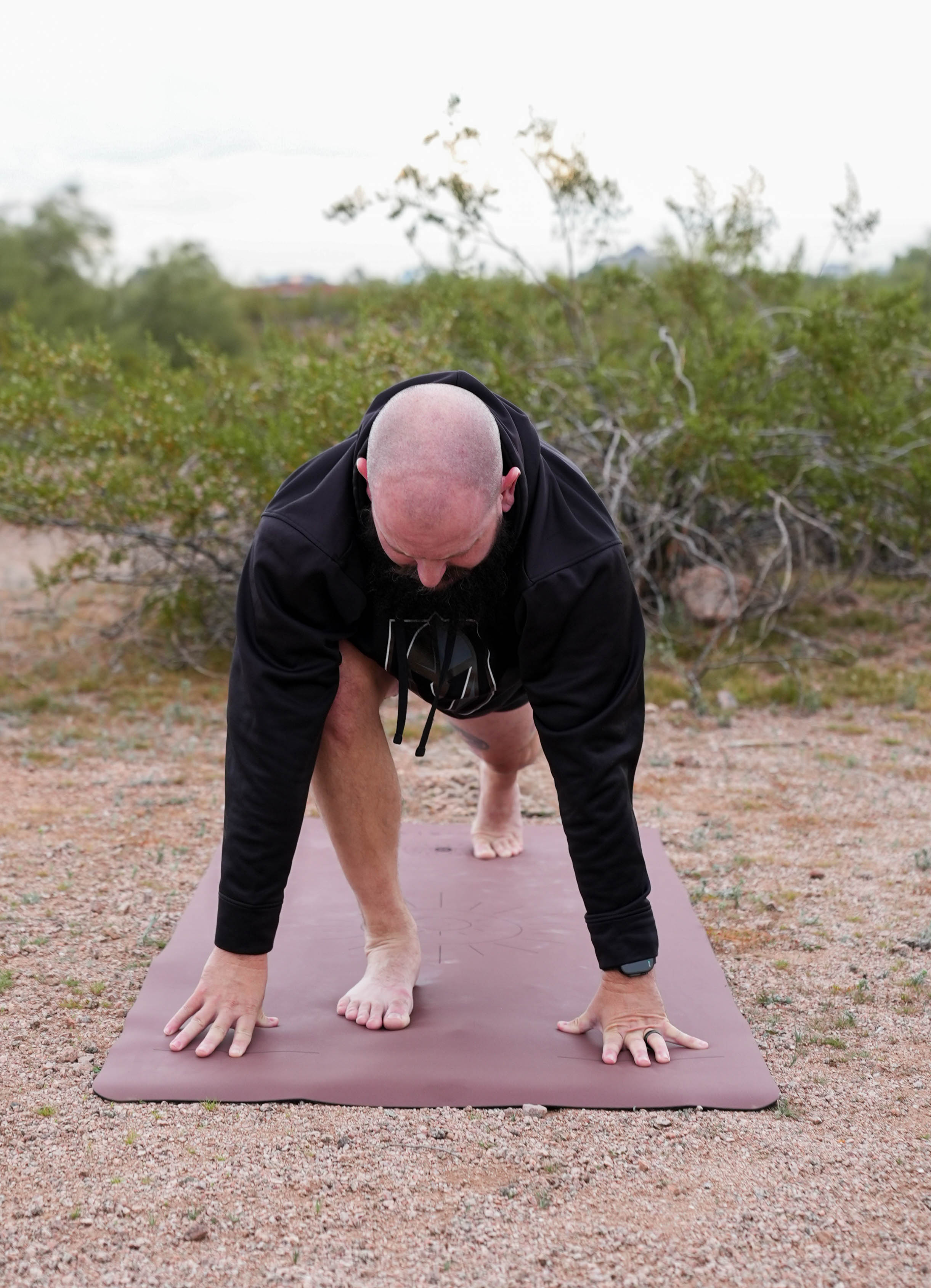 Person in black hoodie and pants on a Red Rocks Sedona extra wide Sonoran Sunset yoga mat outdoors with greenery in the background