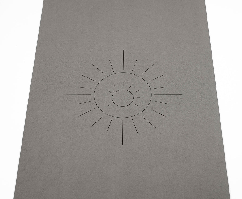 A zoomed in photograph of the yoga mat featuring a simple engraved sun design in the center, Sonoran Sunset, set against a clean white background.