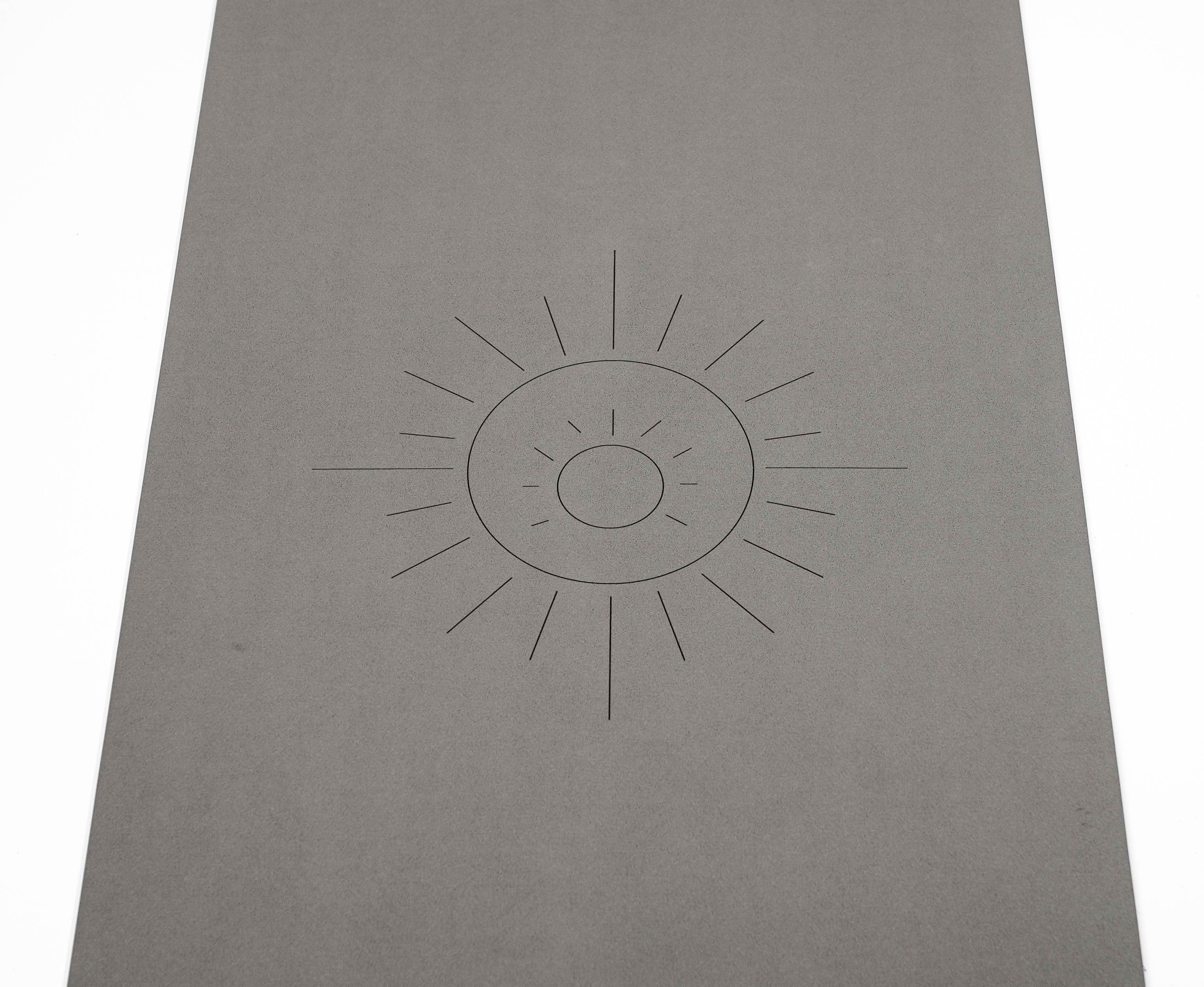 A zoomed in photograph of the yoga mat featuring a simple engraved sun design in the center, Sonoran Sunset, set against a clean white background.